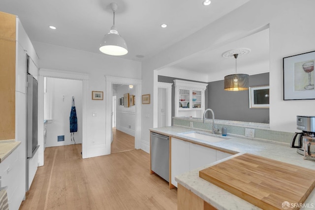 kitchen featuring hanging light fixtures, a sink, white cabinets, dishwasher, and light wood-style floors