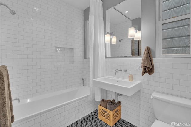 full bathroom featuring toilet, tile walls, tiled shower / bath, and a sink