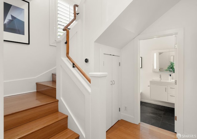 stairs with vaulted ceiling, sink, and hardwood / wood-style floors