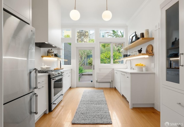 kitchen with decorative light fixtures, white cabinets, ornamental molding, stainless steel appliances, and wall chimney range hood