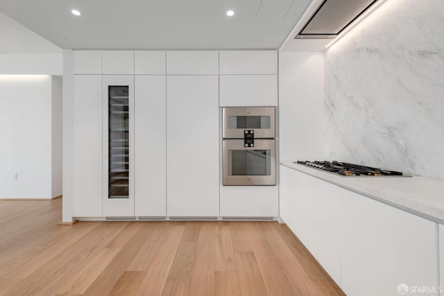 kitchen featuring light wood-type flooring, stainless steel appliances, white cabinets, and light stone counters