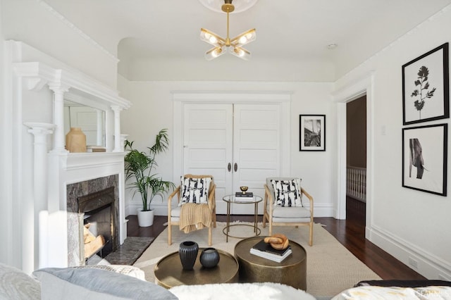 living area featuring a chandelier, dark wood-style flooring, baseboards, and a premium fireplace