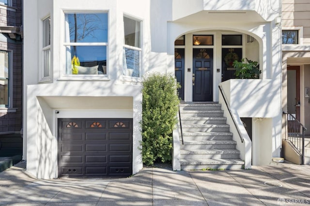 property entrance featuring an attached garage, concrete driveway, and stucco siding