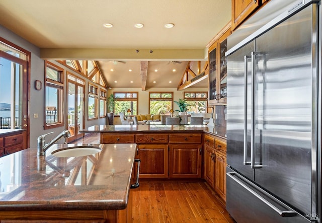 kitchen with sink, vaulted ceiling with beams, high end refrigerator, light hardwood / wood-style flooring, and a kitchen island