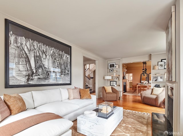 living area with ornamental molding, wood finished floors, and stairway