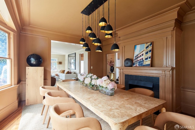 dining area with a healthy amount of sunlight, ornamental molding, a fireplace, and light wood finished floors