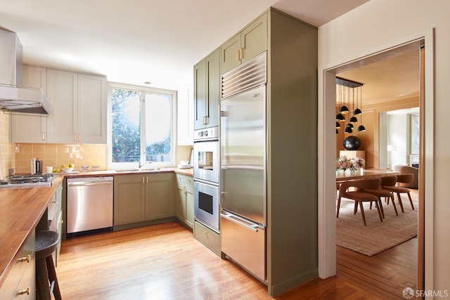 kitchen with wall chimney range hood, decorative backsplash, light wood-style floors, stainless steel appliances, and butcher block countertops