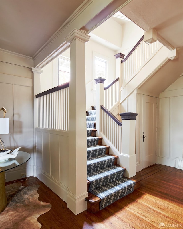 staircase with wood finished floors, crown molding, and a decorative wall