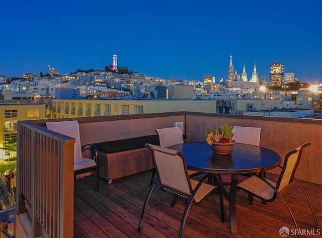 deck at twilight with outdoor dining area and a view of city lights