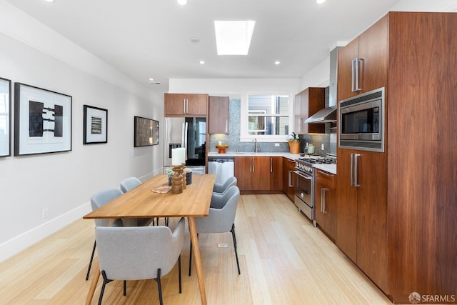 kitchen featuring a sink, tasteful backsplash, stainless steel appliances, light wood-style floors, and a skylight