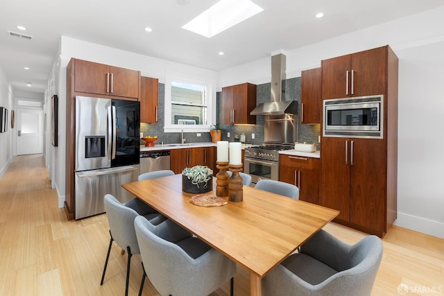 kitchen featuring visible vents, a sink, stainless steel appliances, a skylight, and wall chimney range hood