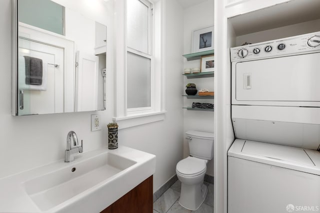 half bathroom featuring toilet, stacked washing maching and dryer, vanity, and baseboards