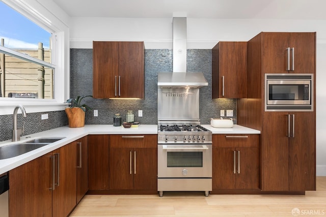 kitchen featuring backsplash, wall chimney range hood, light countertops, stainless steel appliances, and a sink