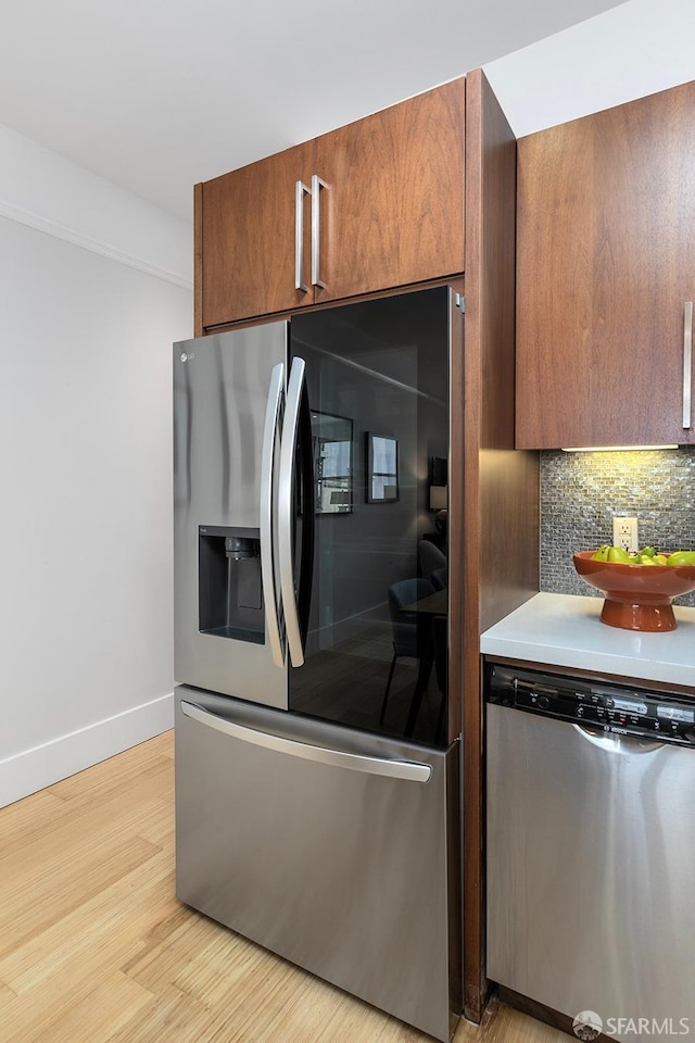 kitchen featuring light wood finished floors, tasteful backsplash, baseboards, brown cabinetry, and stainless steel appliances