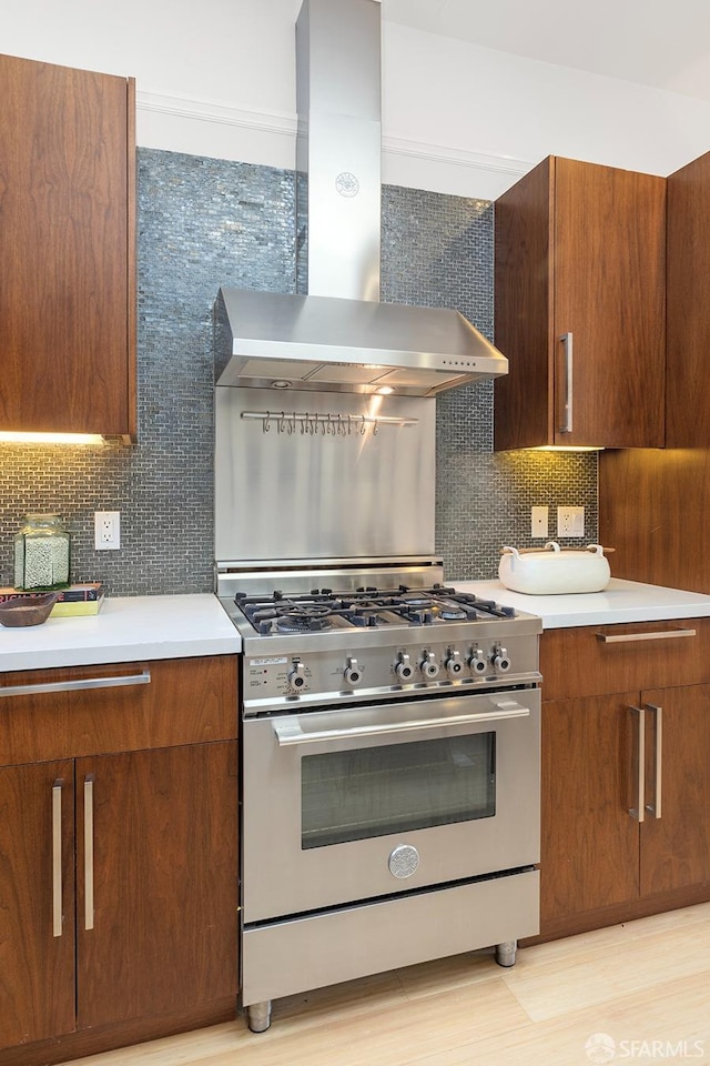 kitchen with stainless steel stove, tasteful backsplash, wall chimney exhaust hood, and light countertops