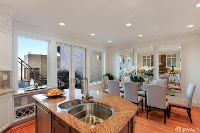 kitchen with light stone countertops, french doors, light wood-type flooring, backsplash, and sink