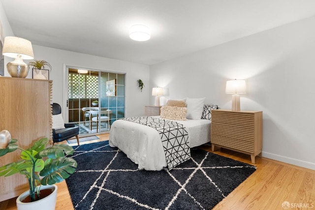 bedroom with baseboards, wood finished floors, and access to outside