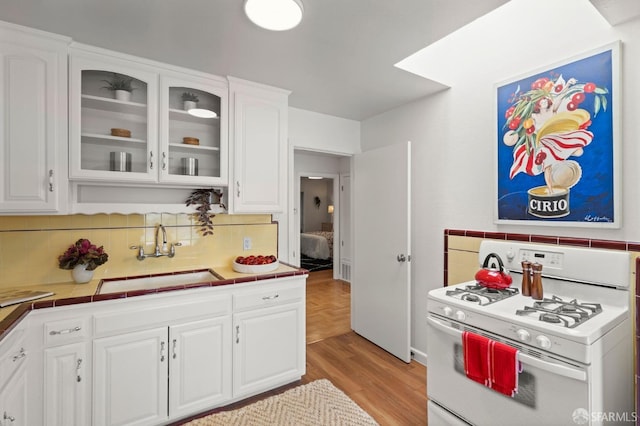 kitchen featuring white cabinetry, tasteful backsplash, a sink, tile counters, and white range with gas cooktop