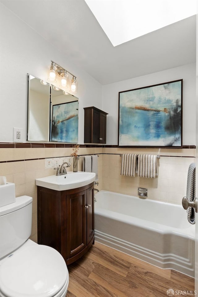 bathroom featuring tile walls, toilet, a garden tub, a skylight, and wood finished floors