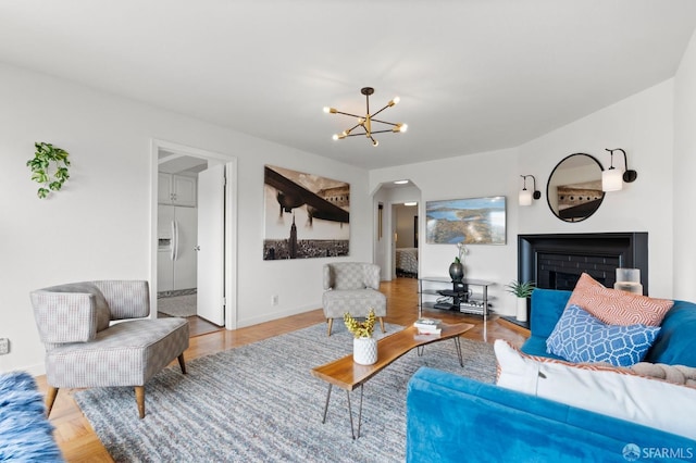 living room featuring a fireplace, arched walkways, a notable chandelier, and baseboards