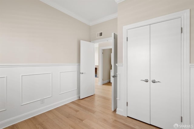 unfurnished bedroom with a wainscoted wall, visible vents, a decorative wall, ornamental molding, and light wood-type flooring