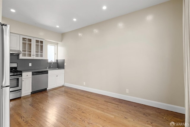 kitchen with appliances with stainless steel finishes, wood finished floors, under cabinet range hood, white cabinetry, and a sink
