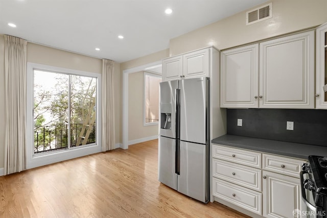 kitchen with visible vents, white cabinets, light wood-type flooring, gas range oven, and stainless steel fridge