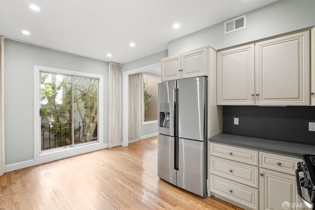 kitchen featuring light wood-style floors, stove, visible vents, and stainless steel fridge with ice dispenser