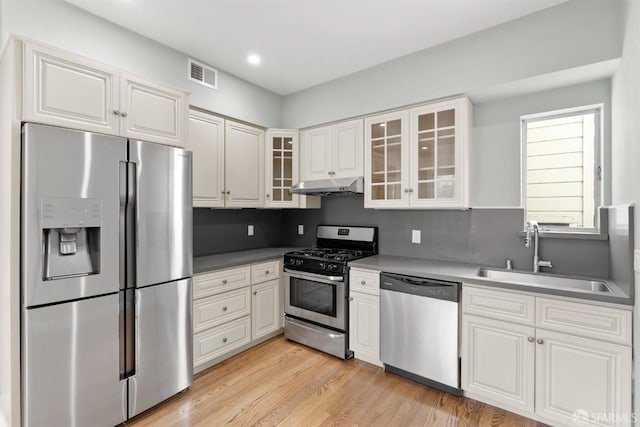 kitchen featuring light wood-style flooring, under cabinet range hood, a sink, visible vents, and appliances with stainless steel finishes