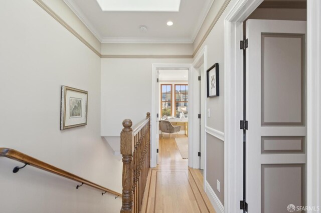 hallway featuring a skylight, an upstairs landing, light wood-style floors, and ornamental molding