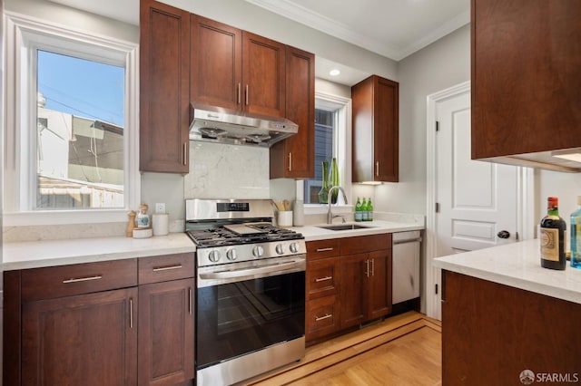 kitchen featuring light wood finished floors, a sink, ornamental molding, stainless steel appliances, and under cabinet range hood