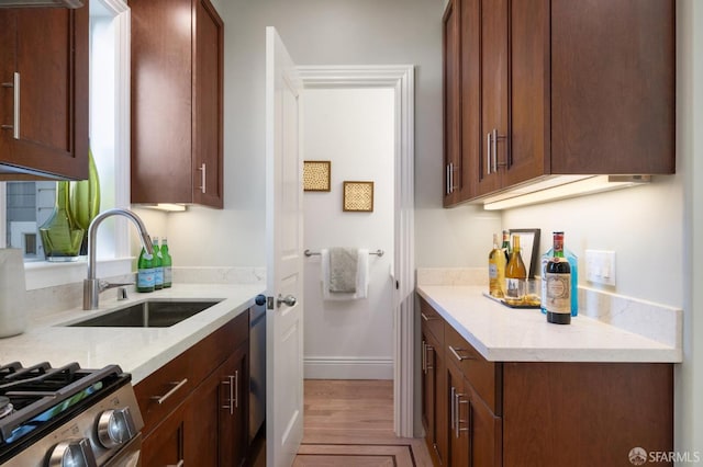 kitchen featuring stove, light stone countertops, baseboards, and a sink