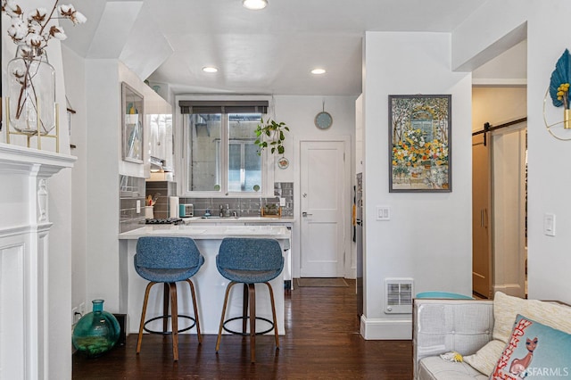 kitchen with white cabinets, dark wood-type flooring, a barn door, decorative backsplash, and a breakfast bar area