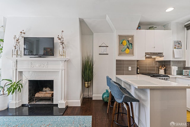 kitchen featuring kitchen peninsula, dark hardwood / wood-style flooring, backsplash, white cabinets, and a breakfast bar