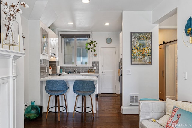 kitchen with dark hardwood / wood-style flooring, white cabinets, tasteful backsplash, a barn door, and a breakfast bar