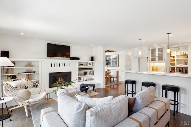 living room with crown molding, recessed lighting, a glass covered fireplace, and dark wood finished floors