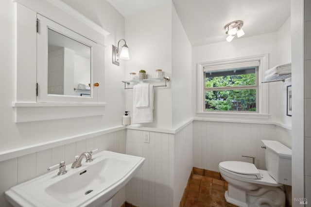 bathroom featuring toilet, a sink, and a wainscoted wall