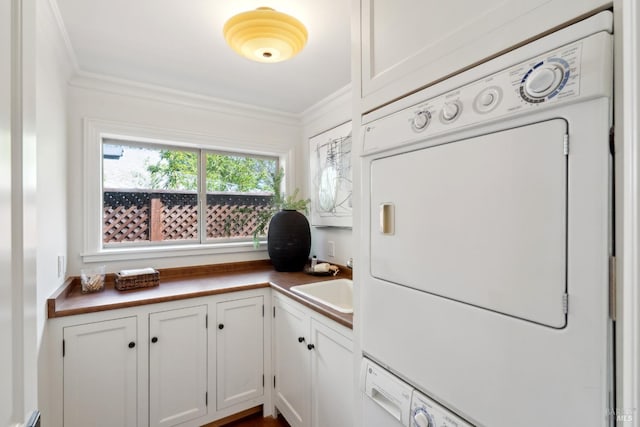 clothes washing area with crown molding, stacked washer and clothes dryer, a sink, and cabinet space