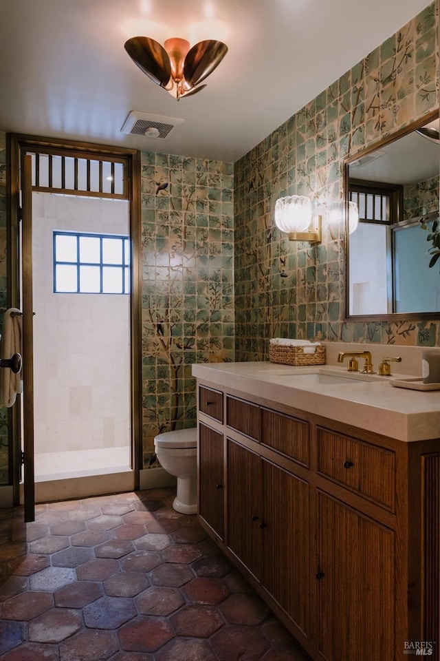 bathroom with toilet, visible vents, tile walls, vanity, and wallpapered walls