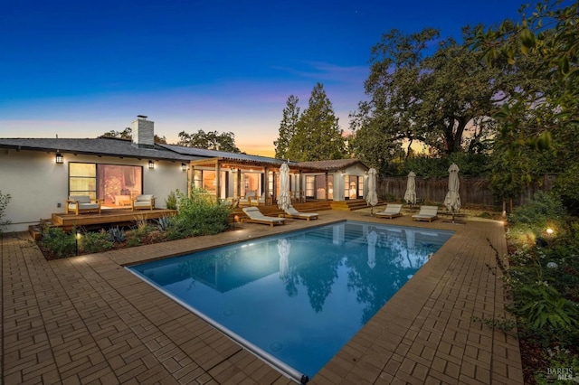 pool at dusk with a fenced in pool, an exterior structure, a patio area, fence, and an outdoor structure