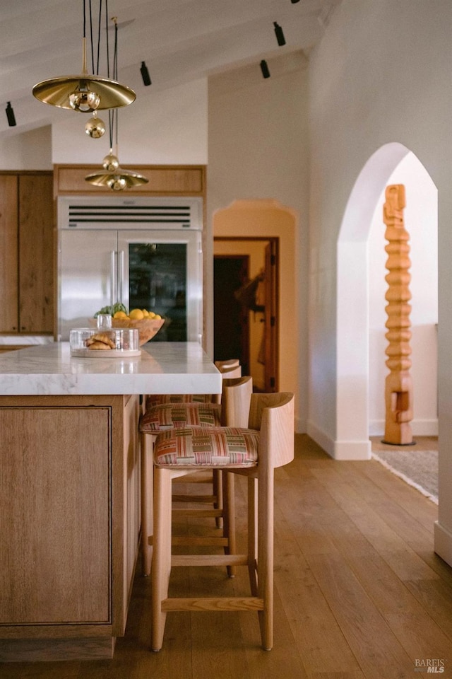 interior space featuring built in fridge, arched walkways, light countertops, high vaulted ceiling, and light wood-type flooring