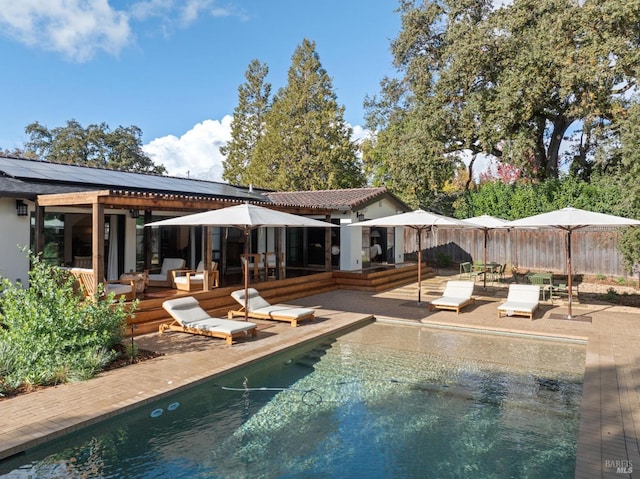 back of property with a patio, solar panels, fence, a wooden deck, and an outdoor pool