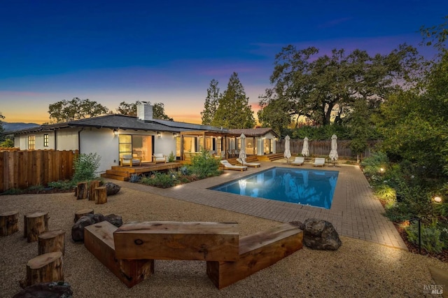 rear view of property with a fenced backyard, a wooden deck, a fenced in pool, a chimney, and a patio area