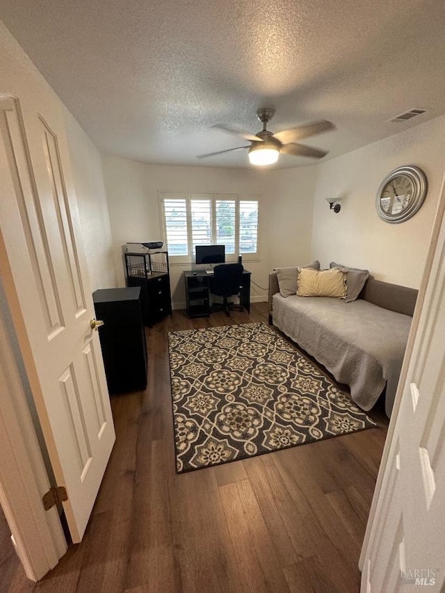 bedroom featuring dark wood-type flooring, a textured ceiling, and ceiling fan