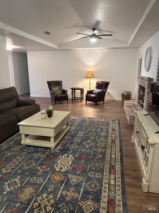 living room with dark wood-type flooring, a fireplace, a textured ceiling, and ceiling fan