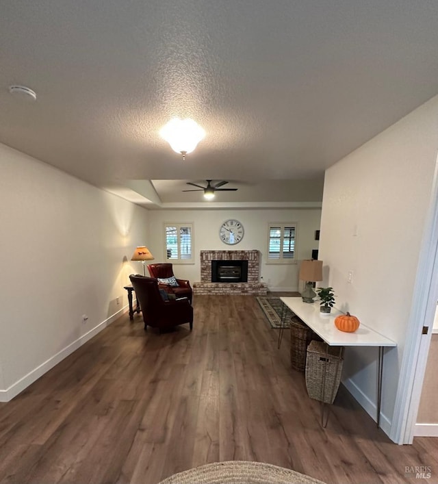 living room featuring a brick fireplace, a textured ceiling, dark hardwood / wood-style floors, and ceiling fan