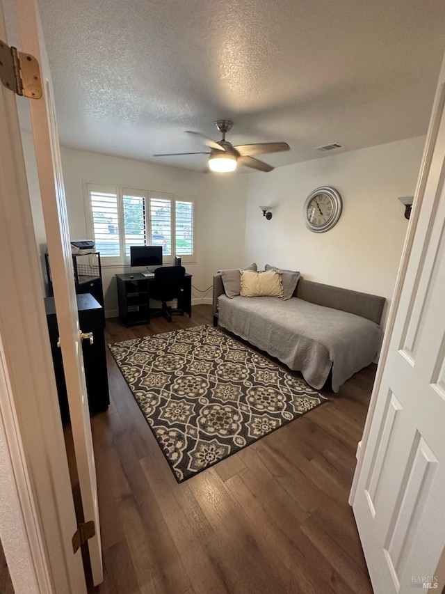 bedroom with dark wood-type flooring, a textured ceiling, and ceiling fan