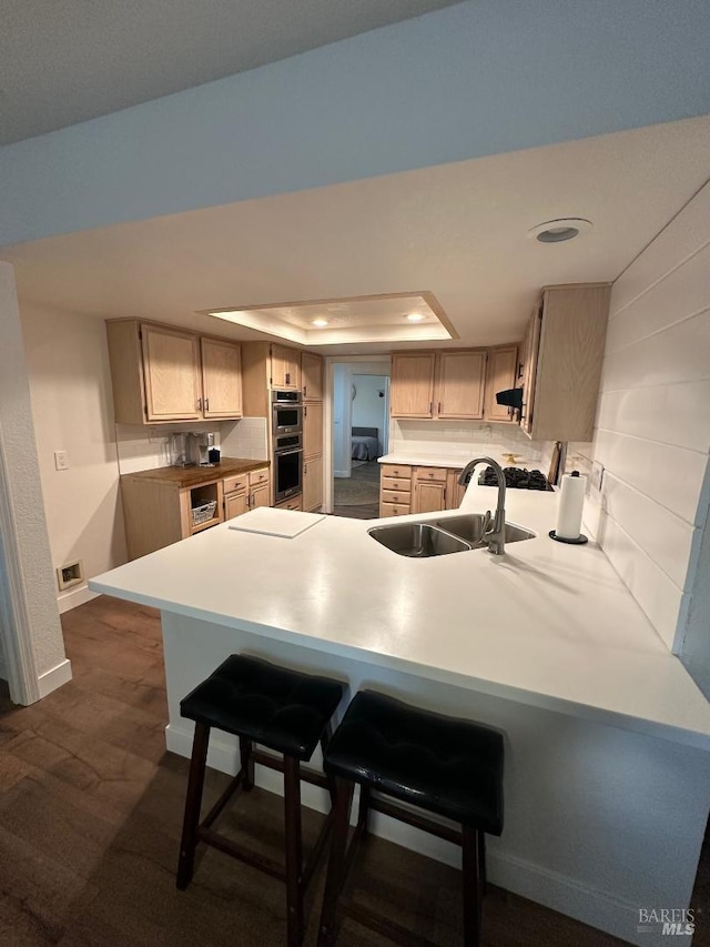 kitchen with light brown cabinets, stainless steel double oven, a tray ceiling, and sink