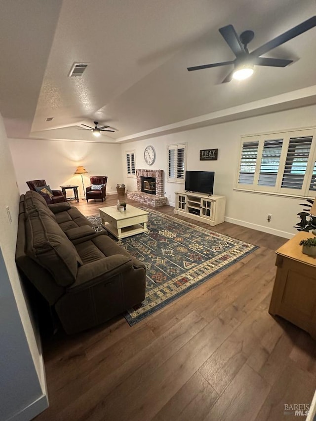 living room featuring dark wood-type flooring, a fireplace, and ceiling fan