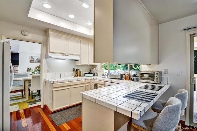 3410 Big Oak Ct, Hayward, CA 94542 - kitchen featuring under cabinet range hood, freestanding refrigerator, dark wood-style flooring, a peninsula, and tile countertops